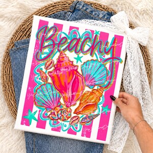 Op de afbeelding: Canvas print met het woord "Beachy" in turquoise en gouden script, met kleurrijke schelpen in roze, oranje en turquoise tinten. De achtergrond heeft roze en witte strepen. De print wordt door een persoon vastgehouden.