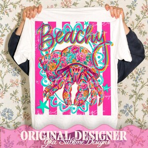 May include: White t-shirt with a vibrant graphic featuring a floral-patterned hermit crab and the word "Beachy" in a colorful script. The design includes pink stripes, teal accents, and stars, creating a summery vibe.