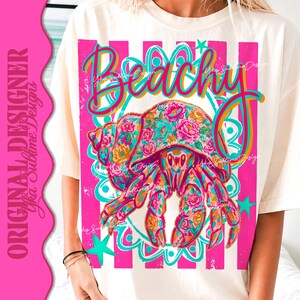 May include: Cream-colored t-shirt with a vibrant graphic featuring a floral-patterned hermit crab and the word "Beachy" in colorful script. The design includes pink stripes and teal accents, creating a summery vibe.