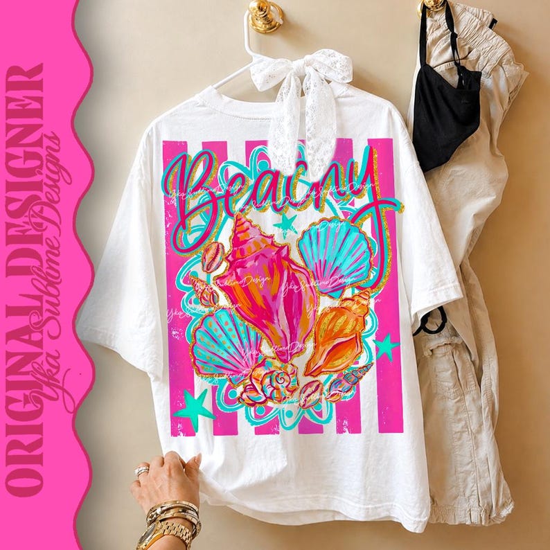 Op de afbeelding: Wit T-shirt met een kleurrijke strandthema-afbeelding. Het ontwerp toont schelpen in roze, oranje en blauwe tinten, met het woord "Beachy" in een scriptlettertype. Roze verticale strepen en sterren maken het ontwerp compleet.
