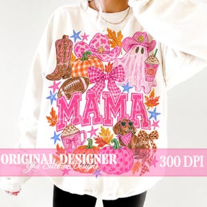 May include: A cream-colored sweatshirt featuring a colorful graphic print with the word MAMA in large pink letters. The design includes a brown cowboy boot, a pink cowgirl hat, a ghost, a dachshund, pumpkins, a football, and a pink bow.