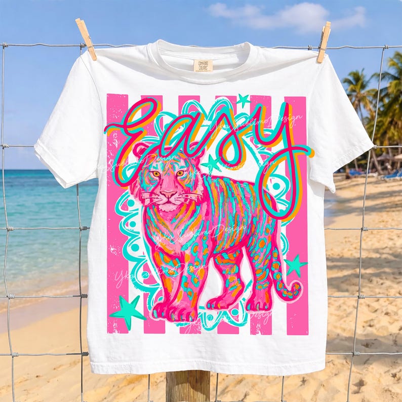 May include: White t-shirt with a colorful tiger graphic. The tiger is depicted in shades of pink, blue, and orange, with the word "EASY" in a vibrant script above it. The design includes pink stripes and teal stars.