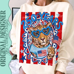 Op de afbeelding: Cr&egrave;mekleurige sweatshirt met een luipaard met hartvormige blauwe bril en een Amerikaanse vlag. Het ontwerp bevat de tekst "250 YEARS" in blauw, tegen een rood, wit en blauwe patriottische achtergrond.