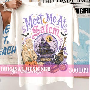 May include: A cream-coloured t-shirt featuring a graphic print with the text 'Meet Me At Salem'. The design includes a purple crystal ball with a haunted house, a witch on a broom, a black cat, a pumpkin, an open spellbook, and a potion bottle.