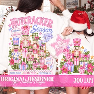 May include: A white sweatshirt featuring a colorful graphic of multiple nutcrackers, poinsettias, and gift boxes. The text reads Nutcracker Season, Christmas Sweet Christmas, Holiday Cheer, and Believe in the Magic in pink and blue lettering.