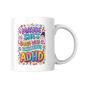 May include: White ceramic mug featuring a vibrant design with the text "MAYBE SHE'S BORN WITH IT MAYBE IT'S ADHD". The design uses multiple colours and fonts. The mug has a white handle and is suitable for hot or cold drinks.