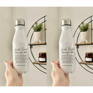 以下が含まれることがあります： シルバーの蓋が付いた白い断熱ウォーターボトル。ボトルには「Work Friend」の文字と定義が印刷されています。ボトルは人の手で持たれています。
