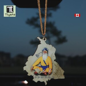 Puede incluir: Un colgante con una figura religiosa con vestimenta amarilla y azul, sentado y leyendo un libro. El colgante tiene forma de mapa y está suspendido de una cadena dorada. El texto "Tlysta" es visible en la esquina superior izquierda.
