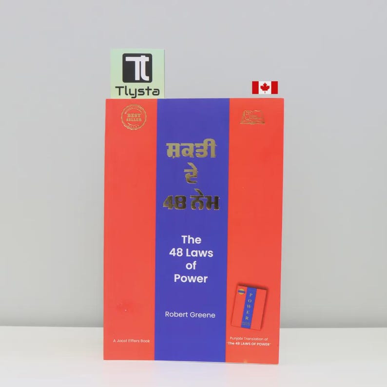 May include: A hardback book titled "The 48 Laws of Power" by Robert Greene. The book has a red cover with a blue vertical stripe and gold lettering. The book also has text in a different language.