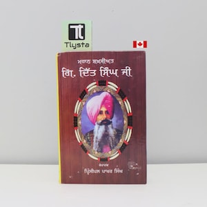 May include: A hardcover book with a portrait of a man in a pink turban and a long white beard. The book has text in a foreign language and a decorative border around the portrait. The cover is a dark brown color.