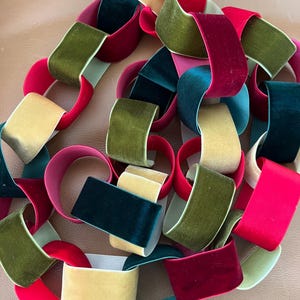 May include: A close-up of a chain made from velvet ribbons in various colours, including red, green, yellow, and teal. The ribbons are linked together, forming a decorative chain. The velvet has a soft, plush texture.