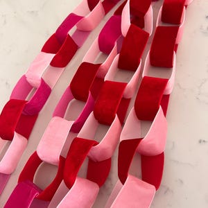 May include: Close-up of several paper chains in shades of pink and red. The chains are made of velvet and are linked together. The chains are arranged diagonally across the frame.