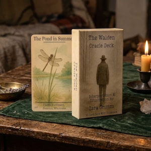 Może przedstawiać: Talia kart wróżebnych "The Walden Oracle Deck" i karta zatytułowana "The Pond in Summer" są wyświetlane na stole. Pudełko talii zawiera ilustrację osoby w kapeluszu. Na stole znajdują się również zapalona świeca, kryształy i miska z ziołami.