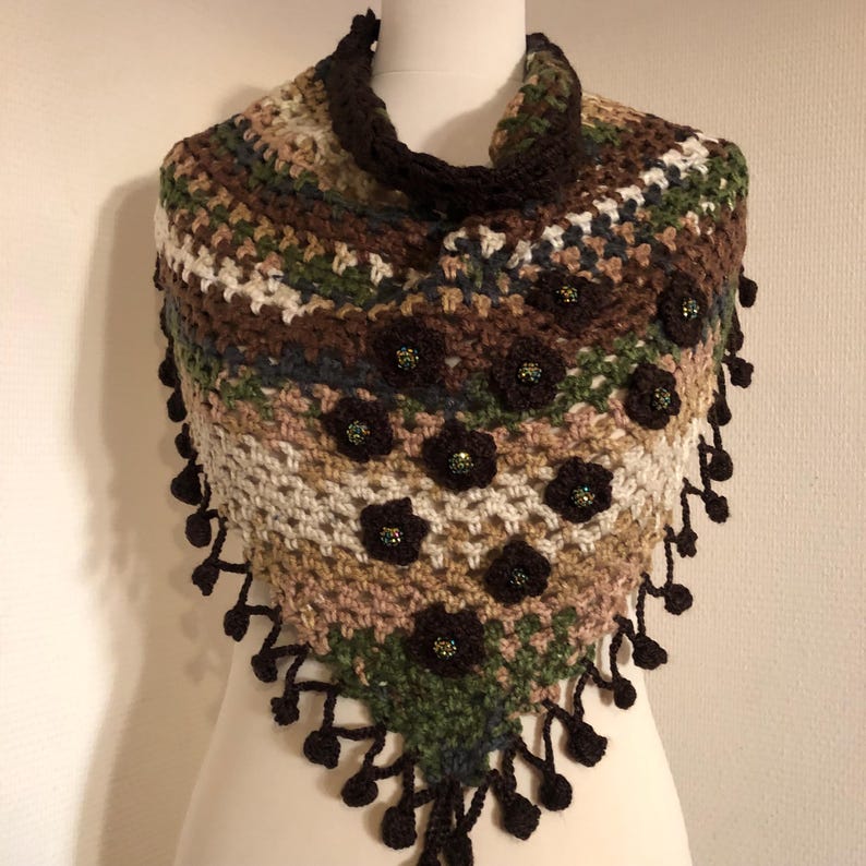 May include: A handmade crochet shawl in shades of brown, green, and cream, decorated with dark brown flower appliqu&eacute;s and beaded centres. The shawl has a triangular shape with a dark brown collar and fringe.