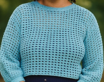 Könnte beinhalten: Hellblauer, offen gewebter Häkelpullover mit Dreiviertelärmeln. Der Pullover wird mit einem dunkelblauen Rock kombiniert. Das Bild ist eine mittlere Aufnahme mit verschwommenem grünem Hintergrund.