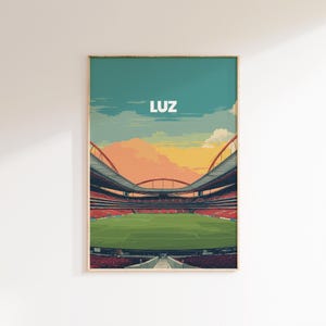 Może przedstawiać: Oprawiony wydruk przedstawiający stadion z zielonym boiskiem, czerwonymi siedzeniami i błękitnym niebem. Słowo "LUZ" jest wydrukowane na górze na biało. Stadion ma zakrzywiony dach i jest osadzony na tle zachodu słońca.