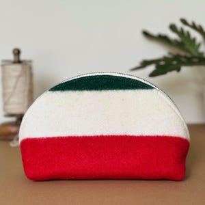 Op de afbeelding: Een halvemaanvormige etui met ritssluiting. De etui is verdeeld in drie horizontale strepen: rood aan de onderkant, wit in het midden en groen aan de bovenkant. De etui is gemaakt van een textuurstof.