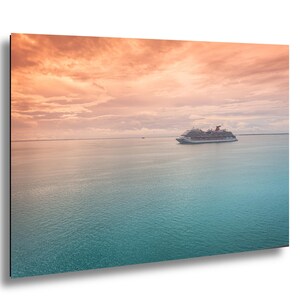 May include: A cruise ship sails on a calm turquoise sea under a vibrant sunset sky. The sky transitions from orange to pink, with soft clouds. The ship is white with red and gray accents, suggesting a vacation theme.
