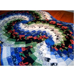 Könnte beinhalten: Ein runder, gesteppter Tischläufer mit einem blauen, grünen, weißen und roten Muster. Die Mitte des Läufers zeigt einen blauen Kreis mit einem weißen Schneeflockenmuster. Der Läufer besteht aus Stoff mit verschiedenen Drucken, darunter Pinguine, Schneeflocken und Weihnachtssterne.