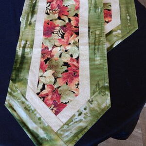 Peut inclure: Un chemin de table vert et blanc avec un motif de feuilles d'automne au centre. Le chemin de table a une forme de diamant avec une bordure blanche et une bordure verte.