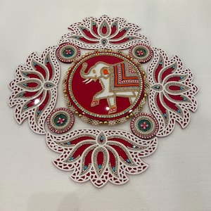 May include: A decorative, red and white wall hanging with an elephant design. The central red circle features a white elephant with orange and gold accents. The design is surrounded by lotus flower shapes and embellished with beads and jewels.