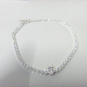 May include: A delicate silver bracelet featuring a series of small, sparkling clear stones. The bracelet has a central decorative element with a larger, round stone. The bracelet is designed to be worn around the wrist.