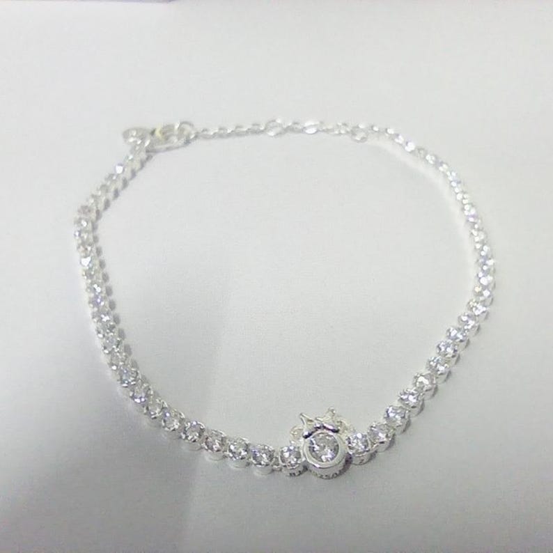 May include: A delicate silver bracelet featuring a series of small, sparkling clear stones. The bracelet has a central decorative element with a larger, round stone. The bracelet is designed to be worn around the wrist.
