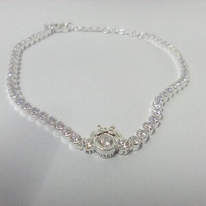May include: A silver bracelet with a series of small, round, clear gemstones. The bracelet has a central design with a larger, round gemstone and a decorative setting. The bracelet is likely made of sterling silver.