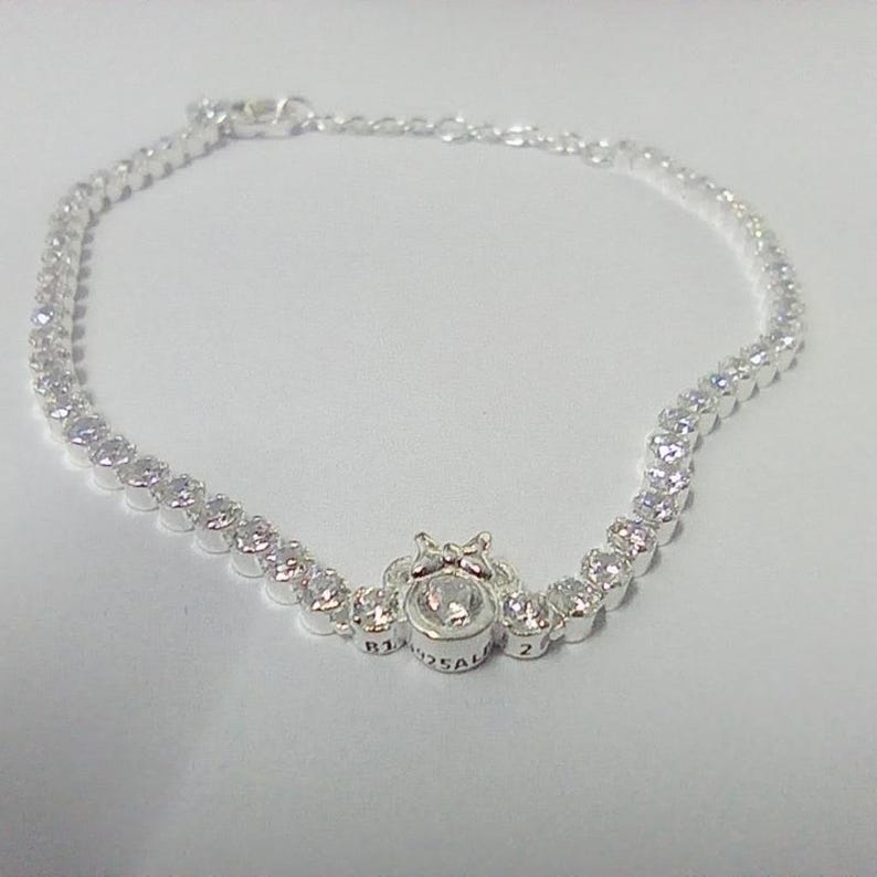 May include: A silver bracelet with a series of small, round, clear gemstones. The bracelet has a central design with a larger, round gemstone and a decorative setting. The bracelet is likely made of sterling silver.