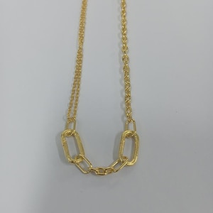 Puede incluir: Un collar dorado con un diseño de cadena. El collar presenta una serie de eslabones ovalados y rectangulares interconectados, creando un aspecto audaz y elegante. La cadena se muestra sobre un fondo blanco liso.