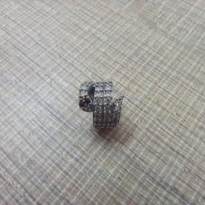Könnte beinhalten: Ein silberfarbener, spiralförmiger Ohrring mit mehreren Reihen kleiner, klarer Edelsteine. Der Ohrring ist auf einer hellbraunen, strukturierten Oberfläche platziert, die sein kompliziertes Design und seine funkelnden Details hervorhebt.