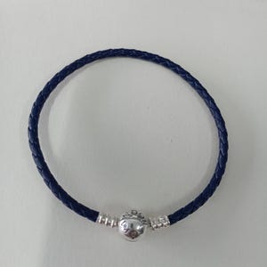 May include: A navy blue braided leather bracelet with a silver clasp. The bracelet is circular. The clasp has a spherical design with engraved details. The bracelet is unworn.