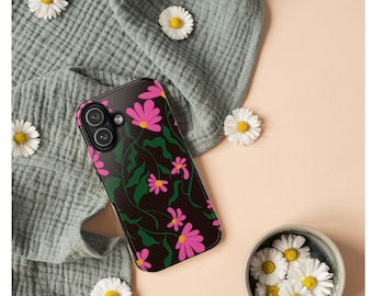 May include: Black phone case with a floral design featuring pink daisies and green stems. The case is on a textured gray fabric with scattered daisies and a small bowl of daisies. The background is a light peach color.