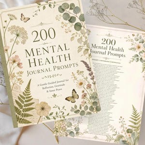 Op de afbeelding: Een journal getiteld 200 Mental Health Journal Prompts met een crèmekleurige kaft voorzien van botanische illustraties van varens, wilde bloemen en vlinders. De tekst luidt A Gentle Guided Journal for Reflection, Gratitude & Inner Peace.