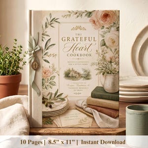Może przedstawiać: Książka kucharska zatytułowana The Grateful Heart Cookbook z kwiatowym wzorem na okładce przedstawiającym róże i zieleń. Książka jest ozdobiona jasną zieloną wstążką i małym krzyżykiem. Tekst zawiera 10 Stron i 21,6 cm na 27,9 cm.
