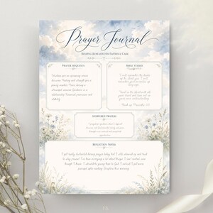 May include: A prayer journal page featuring a sky and cloud background with floral illustrations at the bottom. The text includes Prayer Journal, Resting Beneath Faithful Care, Prayer Requests, Bible Verses, Answered Prayers, and Reflection Notes.