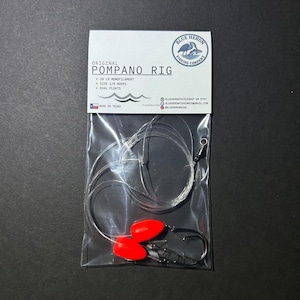 May include: A clear plastic package containing a Pompano fishing rig. The rig includes clear monofilament line, two red oval floats, size 1/0 hooks, and a swivel. The package has a white label with the text "ORIGINAL POMPANO RIG".