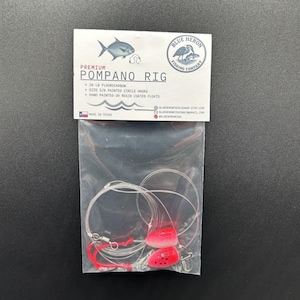 May include: A clear plastic bag containing a Pompano fishing rig. The rig includes a label with the text "Premium Pompano Rig" and "Blue Heron Fishing Company" logo. The rig includes 20 lb fluorocarbon line, size 3/0 painted circle hooks, and hand-painted UV resin coated floats.