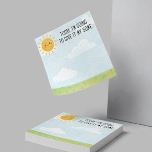 May include: A stack of square sticky notes with a cheerful design. The notes feature a smiling sun, clouds, and a grassy field against a light blue sky. Text on the notes reads, "TODAY, I'M GOING TO GIVE IT MY SOME."
