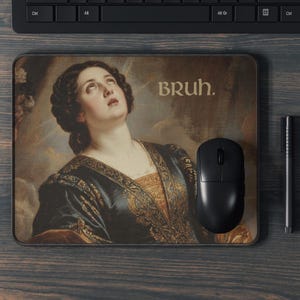 May include: Rectangular mousepad featuring a Renaissance painting of a woman looking upwards, with the word "BRUH." in a sans-serif font. A black computer mouse and pen are next to the mousepad on a wooden surface.