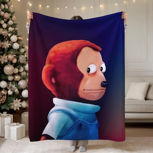 May include: A large, rectangular blanket featuring a cartoon monkey with a side-eye expression. The monkey has red fur, a black nose, and is wearing a blue denim overall. The background transitions from red to dark blue.