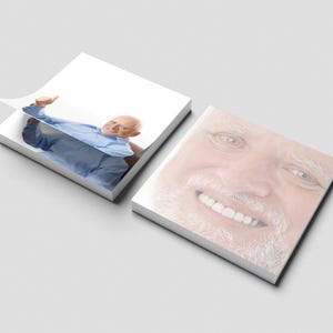 May include: Two white square notepads. One notepad shows a smiling man in a blue shirt, with a corner of the top sheet lifted. The other notepad displays a close-up of the man's smiling face.