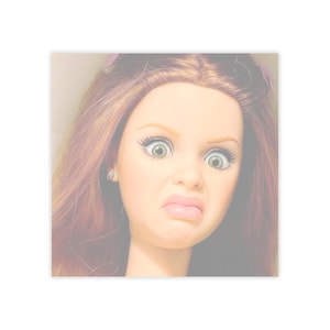 May include: A doll's face with a look of disgust. The doll has light skin, green eyes, and long, auburn hair. The doll's expression includes a wrinkled nose and a downturned mouth. The doll has a small earring in one ear.