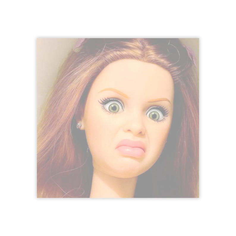 May include: A doll's face with a look of disgust. The doll has light skin, green eyes, and long, auburn hair. The doll's expression includes a wrinkled nose and a downturned mouth. The doll has a small earring in one ear.