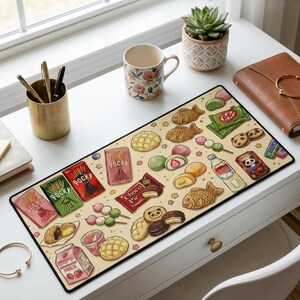 Puede incluir: Alfombrilla de escritorio rectangular con un fondo beige decorado con ilustraciones coloridas de snacks japoneses. El dise&ntilde;o incluye cajas de Pocky, barras Kit Kat, pasteles con forma de pez y mochi. La alfombrilla tiene un borde negro.