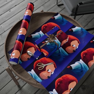 May include: A roll of wrapping paper and a wrapped gift featuring a repeating pattern of a cartoon monkey with red hair and a blue denim jacket on a dark blue background. The gift is tied with a brown ribbon.