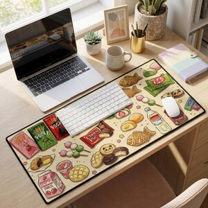 Puede incluir: Alfombrilla de escritorio beige con una colorida ilustraci&oacute;n de aperitivos y dulces japoneses, incluyendo Pocky, Kit Kat y taiyaki. La alfombrilla rectangular, dise&ntilde;ada para teclado y rat&oacute;n, tiene un borde negro y presenta varios alimentos coloridos.