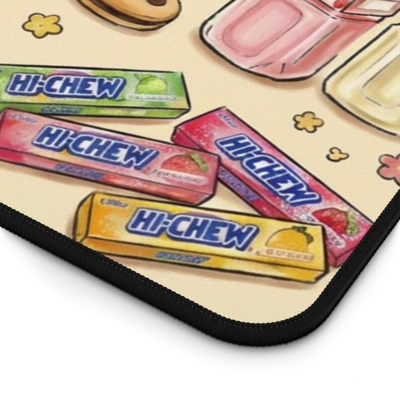 Puede incluir: Primer plano de un mousepad beige con envoltorios de caramelos coloridos. El envoltorio incluye el texto "Hi-Chew" en azul, con sabores como fresa, lima y lim&oacute;n. El mousepad tiene un borde negro y un patr&oacute;n floral.