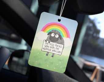 May include: Rectangular air freshener with a cartoon sheep holding a sign that reads "THE LESS FUCKS YOU GIVE, THE HAPPIER YOU LIVE." The design includes a rainbow, clouds, and a green field with white flowers. The air freshener hangs from a string.
