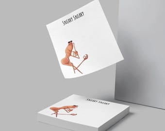 May include: White notepad with the text "SNEAKY SNEAKY" and an illustration of a cartoon shrimp wearing sunglasses. The shrimp is holding a stick and has one leg crossed over the other. A stack of notepads is in the foreground.